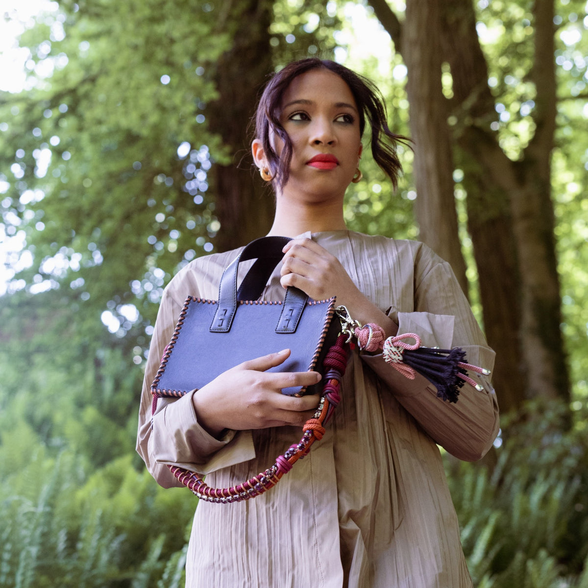 Woman holding a black leather handbag and with a strap with colorful rhinestones in a forest setting