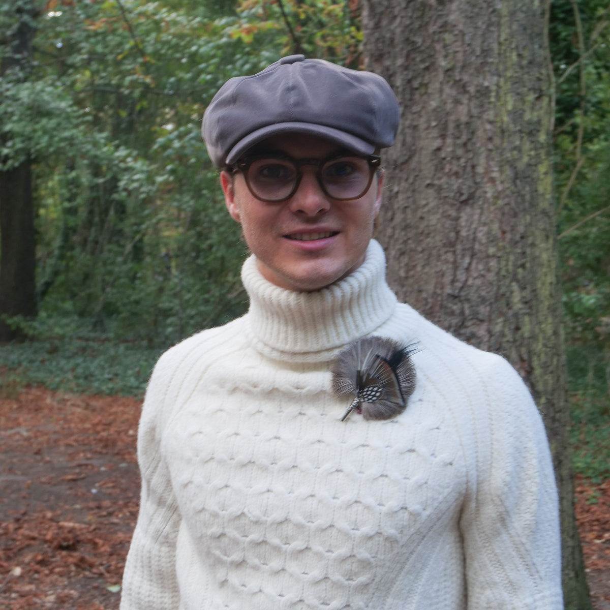 A person wearing pinned to its sweater a feather brooch with black feathers. 