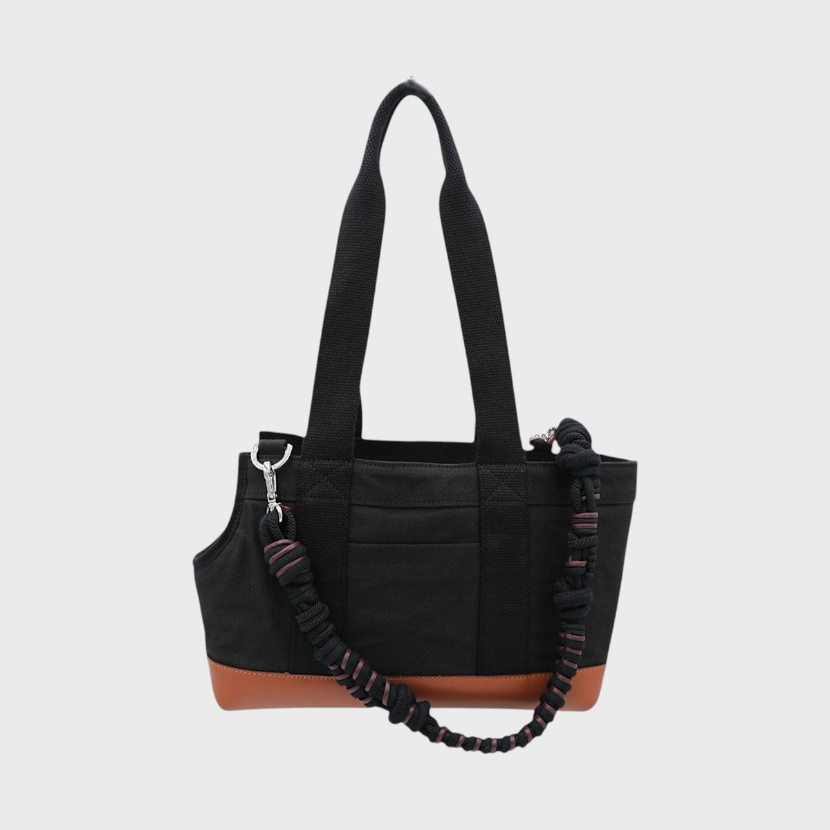 Black dog bag with a brown base on a light gray background, and a black and brown woven macramé bag strap. 