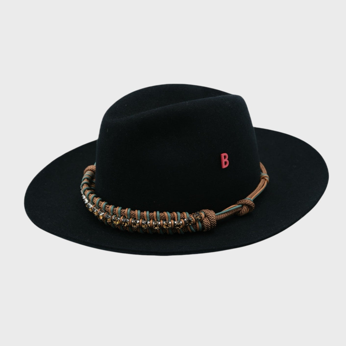 Black fedora hat with a decorative band with green and brown macramé and brown rhinestones on a light gray background