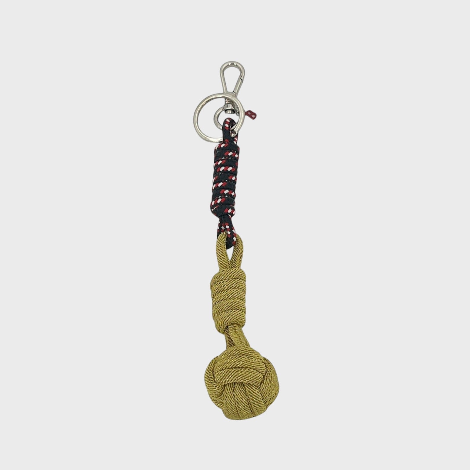 A macramé keychain representing a ball inspired by sailors knots. The straight upper part is dark blue, red and white and the ball part is golden. 