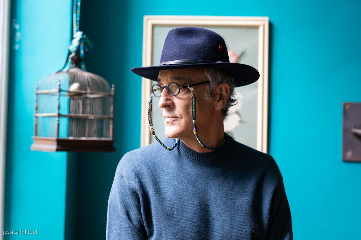 A person wearing a blue hat and glasses,  with a blue and green glasses lanyard. 