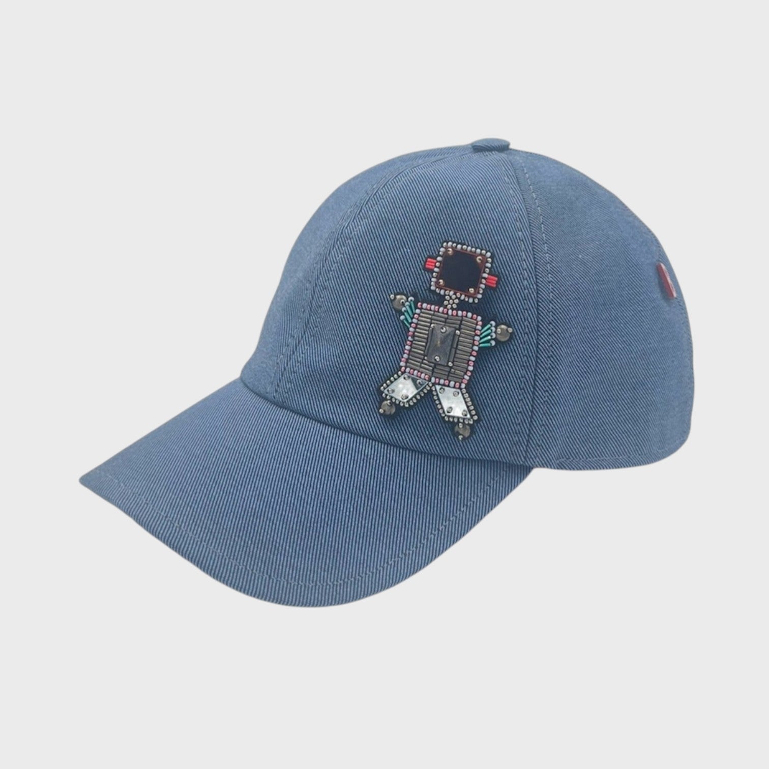 A blue-grey cotton baseball cap with a grey robot brooch pinned on it. 