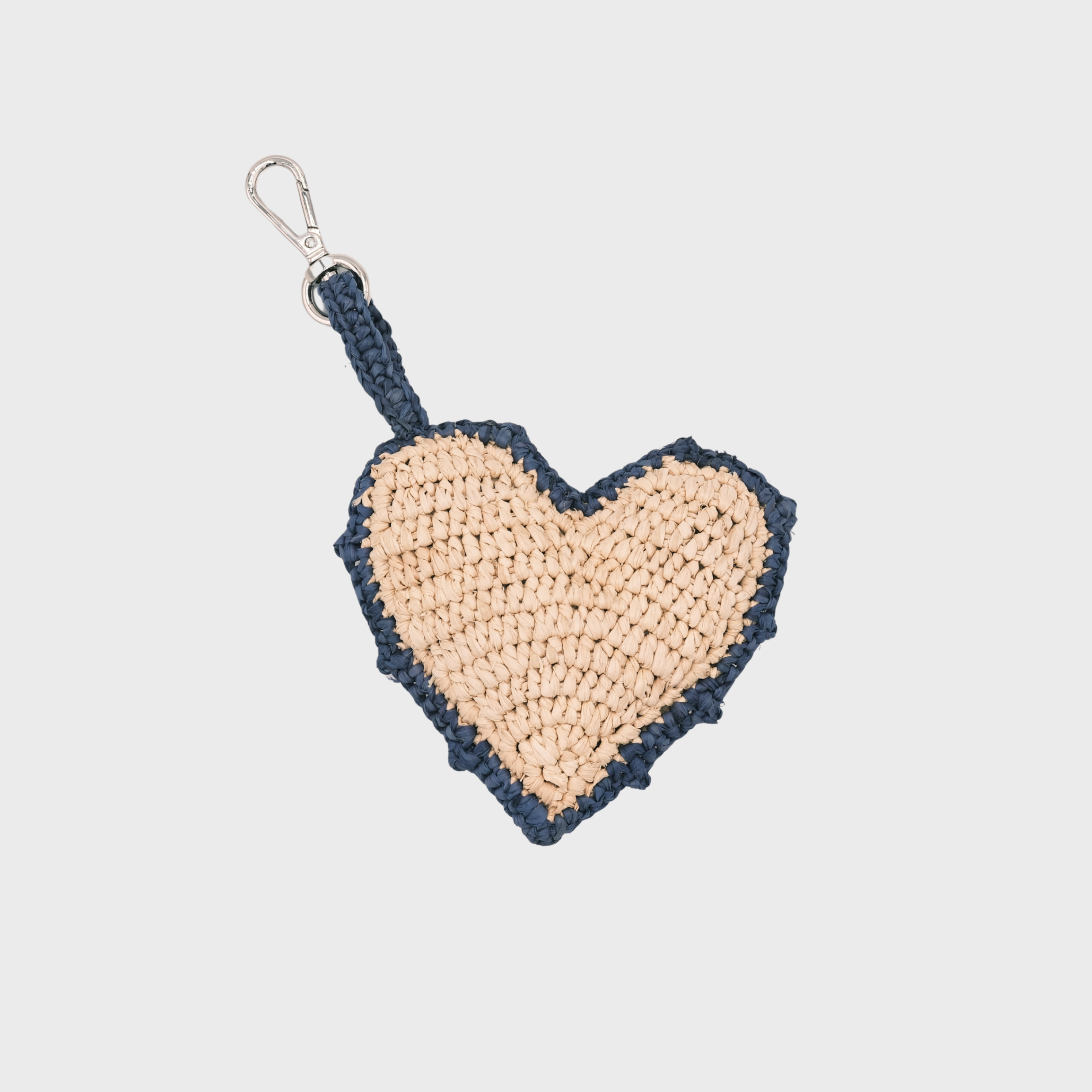 A heart-shaped raffia keychain in beige and navy blue rim, featuring a silver metal clasp.