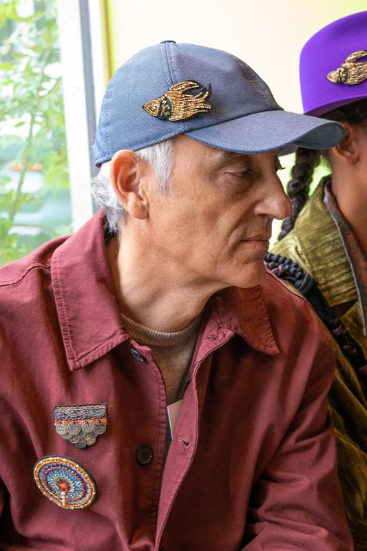 A man wearing a blue jean cotton cap with a golden embroidered brooch on it. 