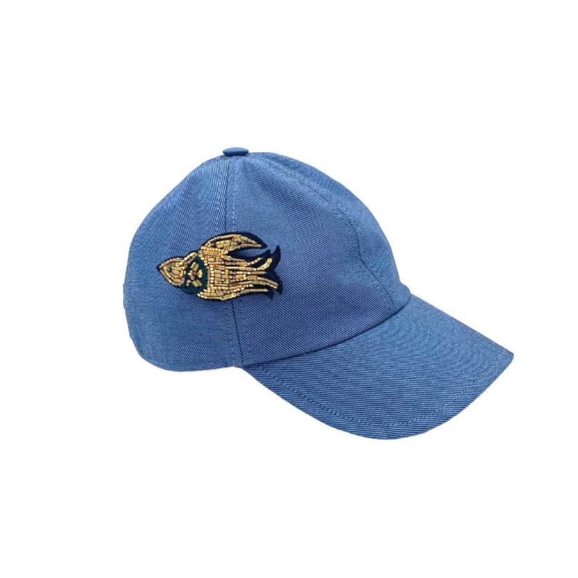 A blue jean cotton cap with a golden embroidered brooch pinned on it representing a bird. 
