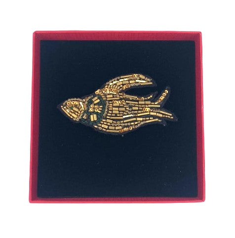 A golden embroidered brooch representing a bird in a red box. 