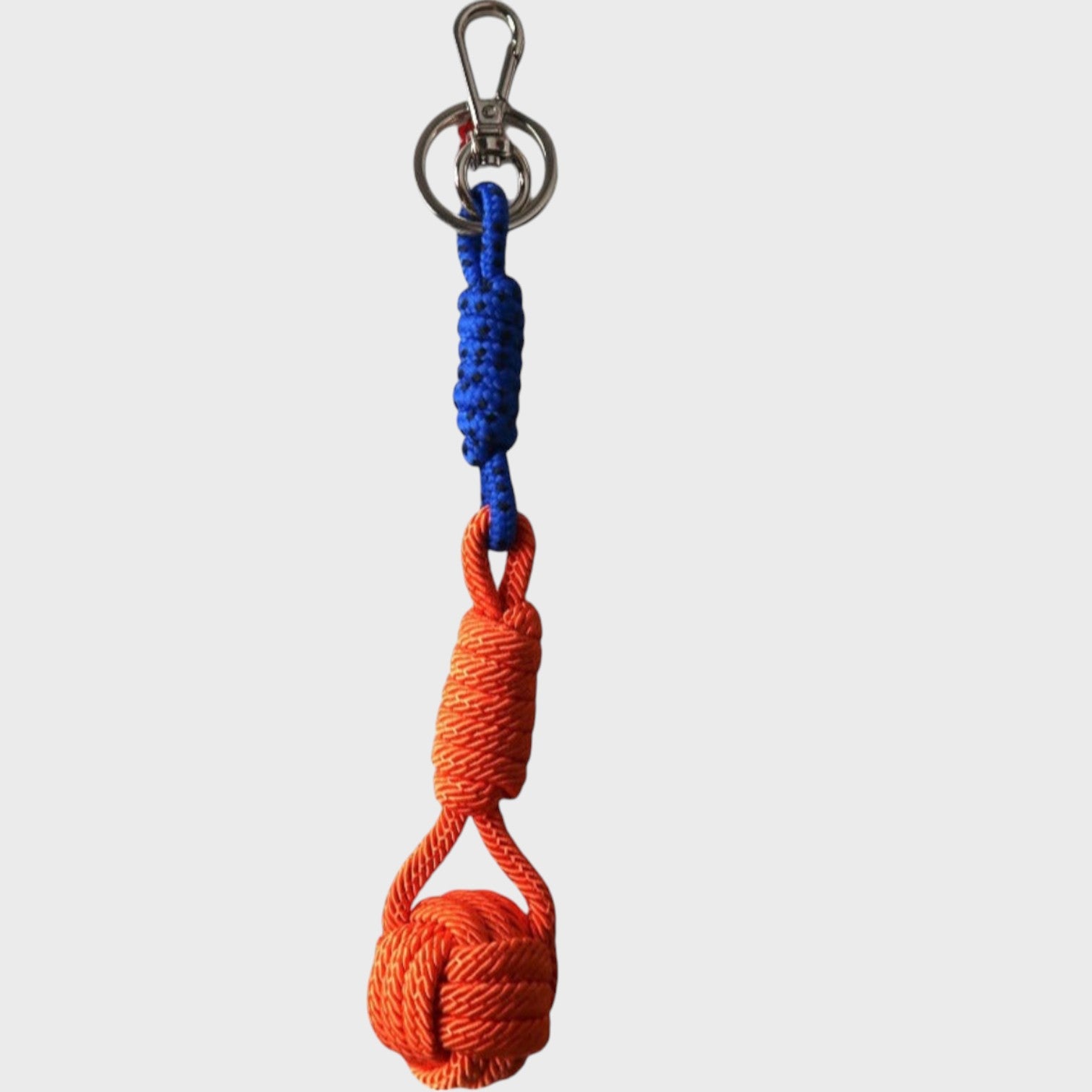 A macramé keychain representing a ball inspired by sailors knots. The straight upper part is blue and black and the ball part is orange. 