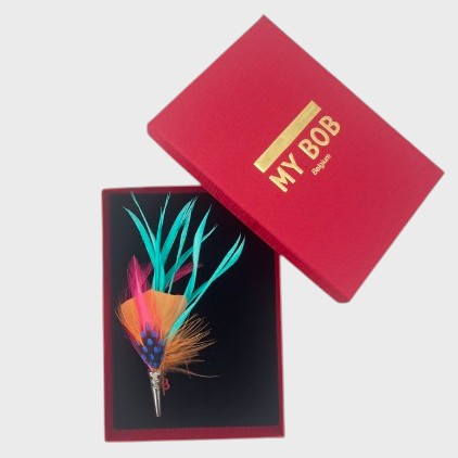 Pink and blue  and orange feather brooch in a box on a light gray background