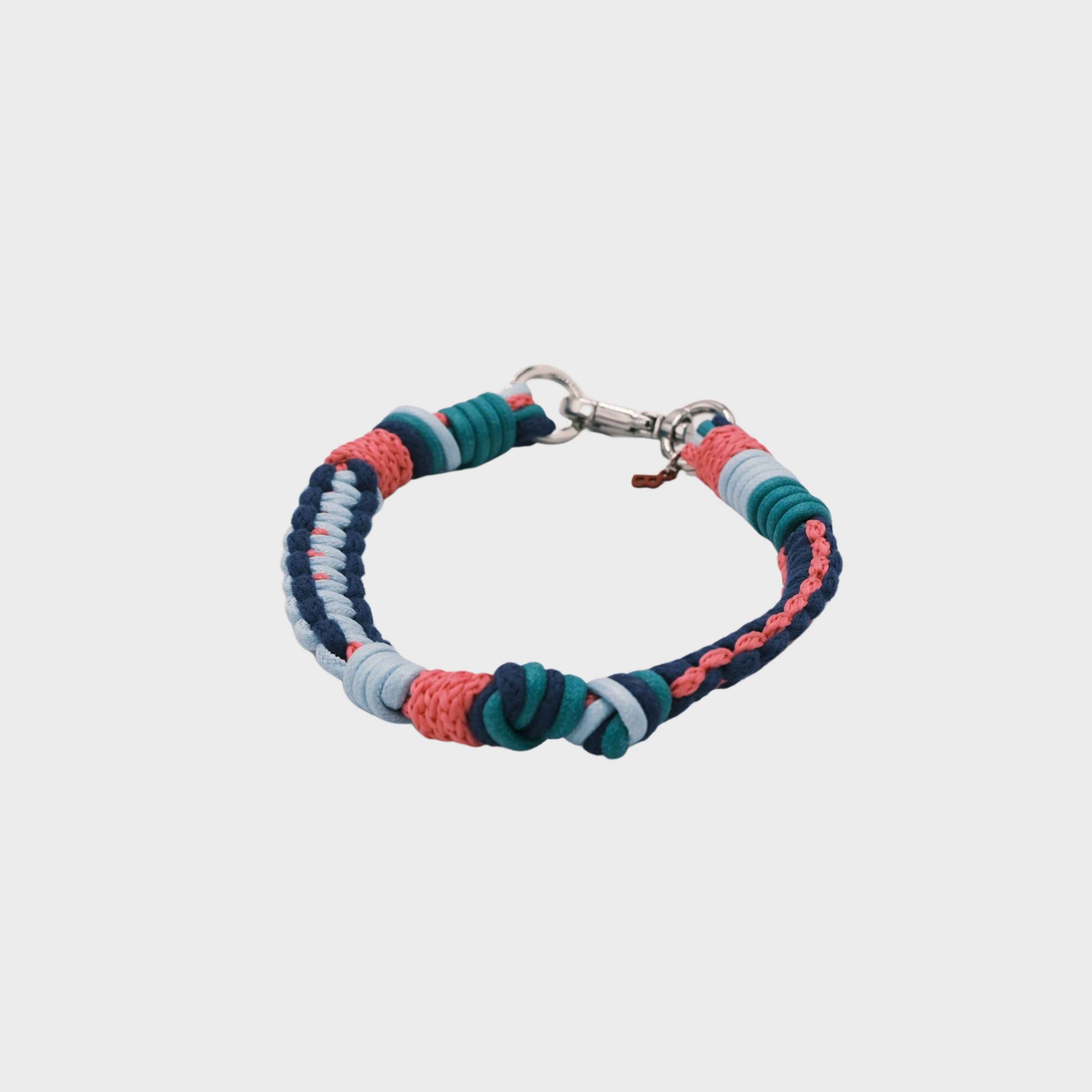 A braided macramé cord collar in shades of bright pink, light blue and dark blue with a silver clasp, centered on a light gray background.