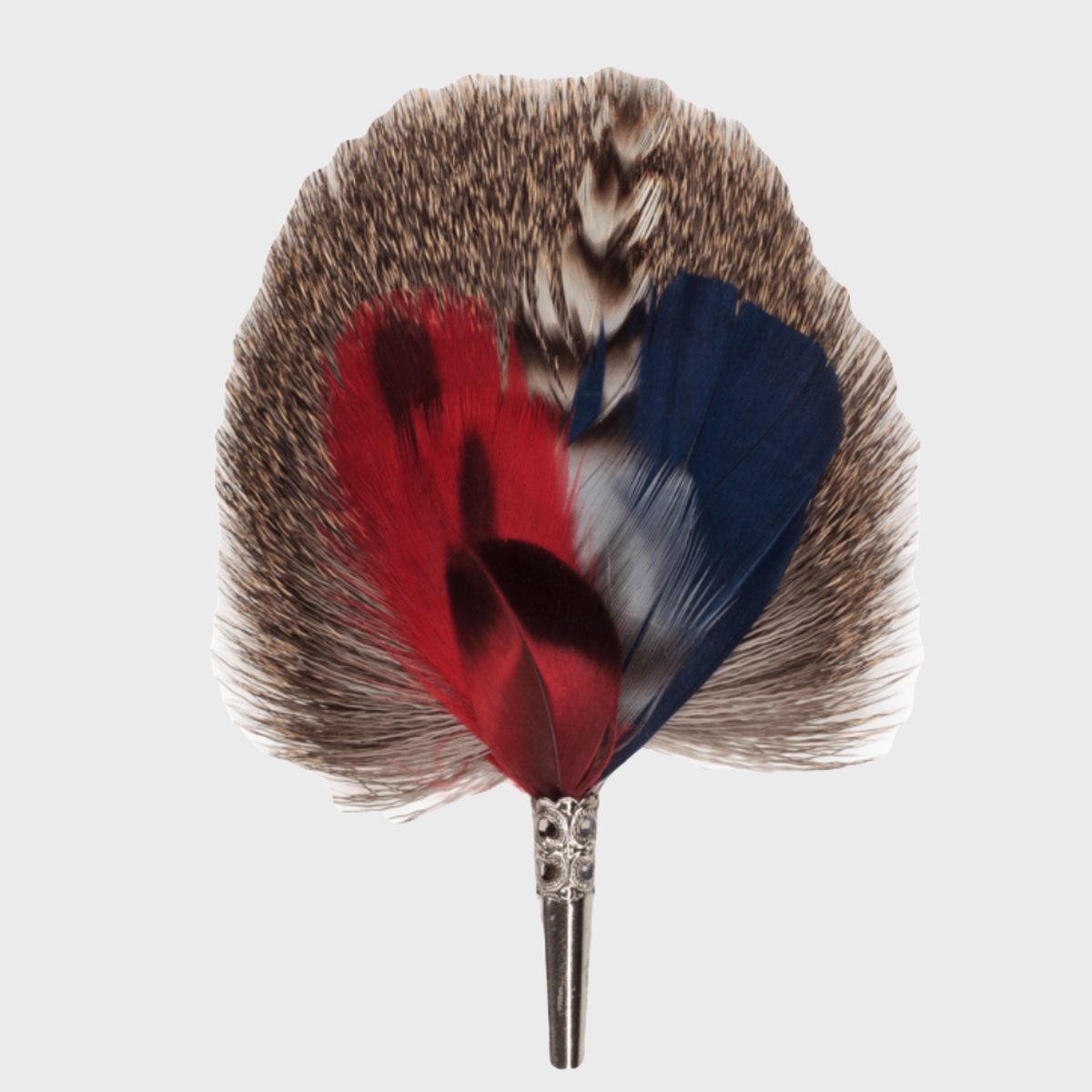 A brooch featuring a combination of red, blue, and brown dyed feathers, with a metallic clasp, handmade in Germany.