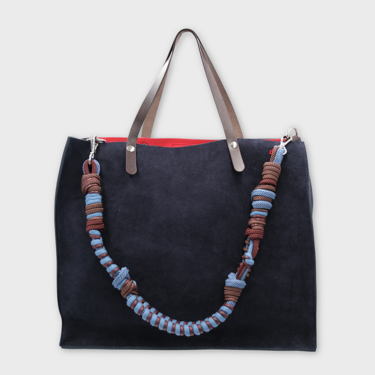 A large dark navy blue suede cabas bag with brown leather handles and a long woven rope shoulder strap in brown, blue, and light blue, shown against a light gray background.