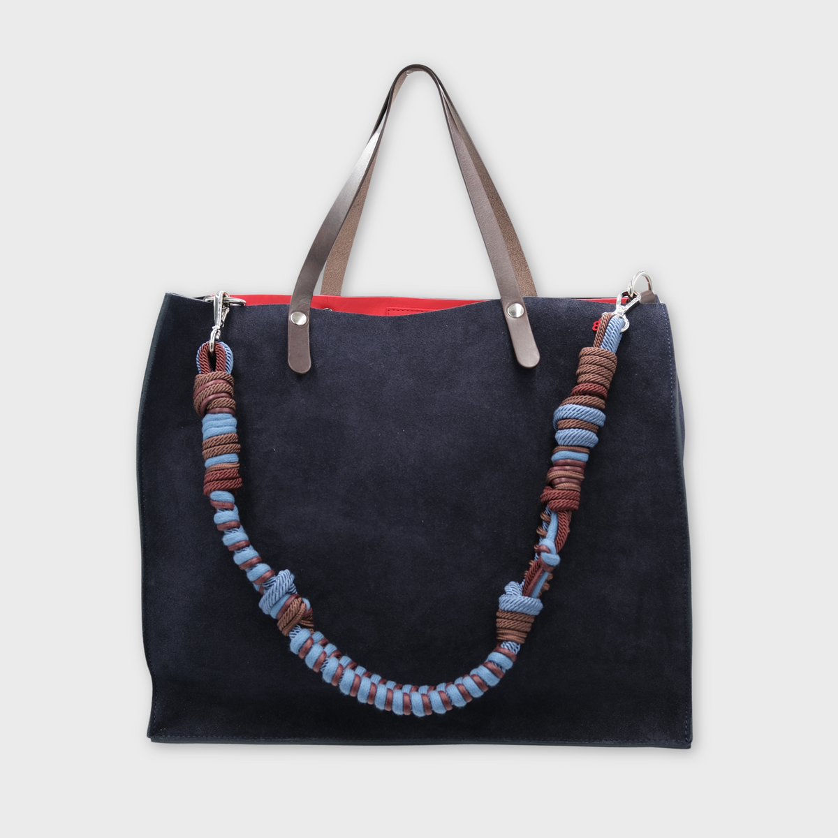 A large dark navy blue suede cabas bag with brown leather handles and a long woven rope shoulder strap in brown, blue, and light blue, shown against a light gray background.