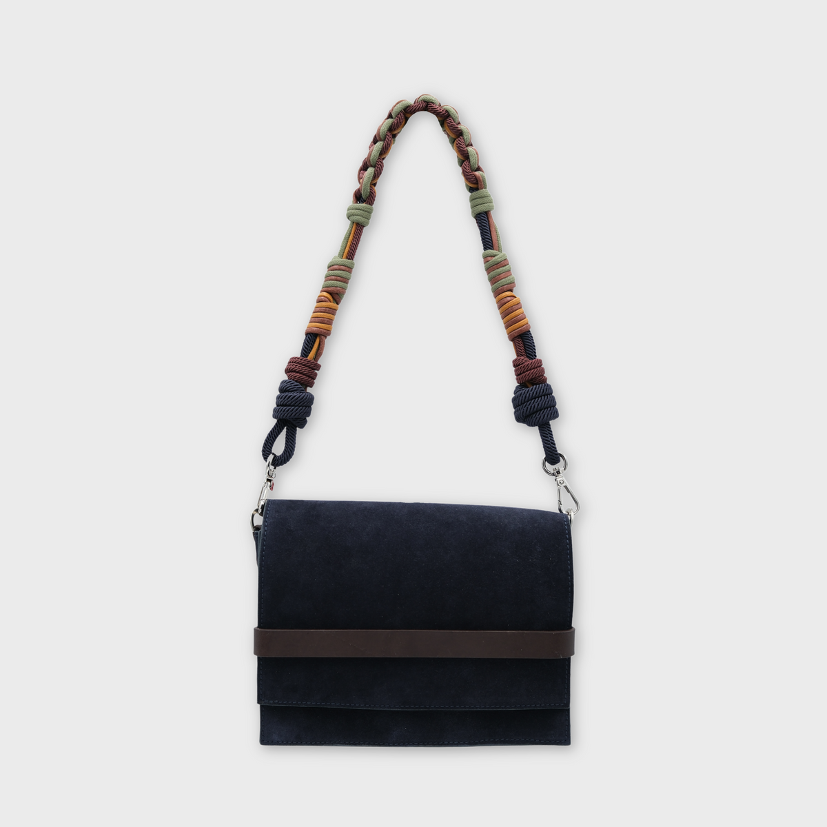 A dark navy blue suede crossbody bag with a brown leather band across the front flap and a long braided shoulder strap featuring multicolored woven accents, shown against a light gray background.