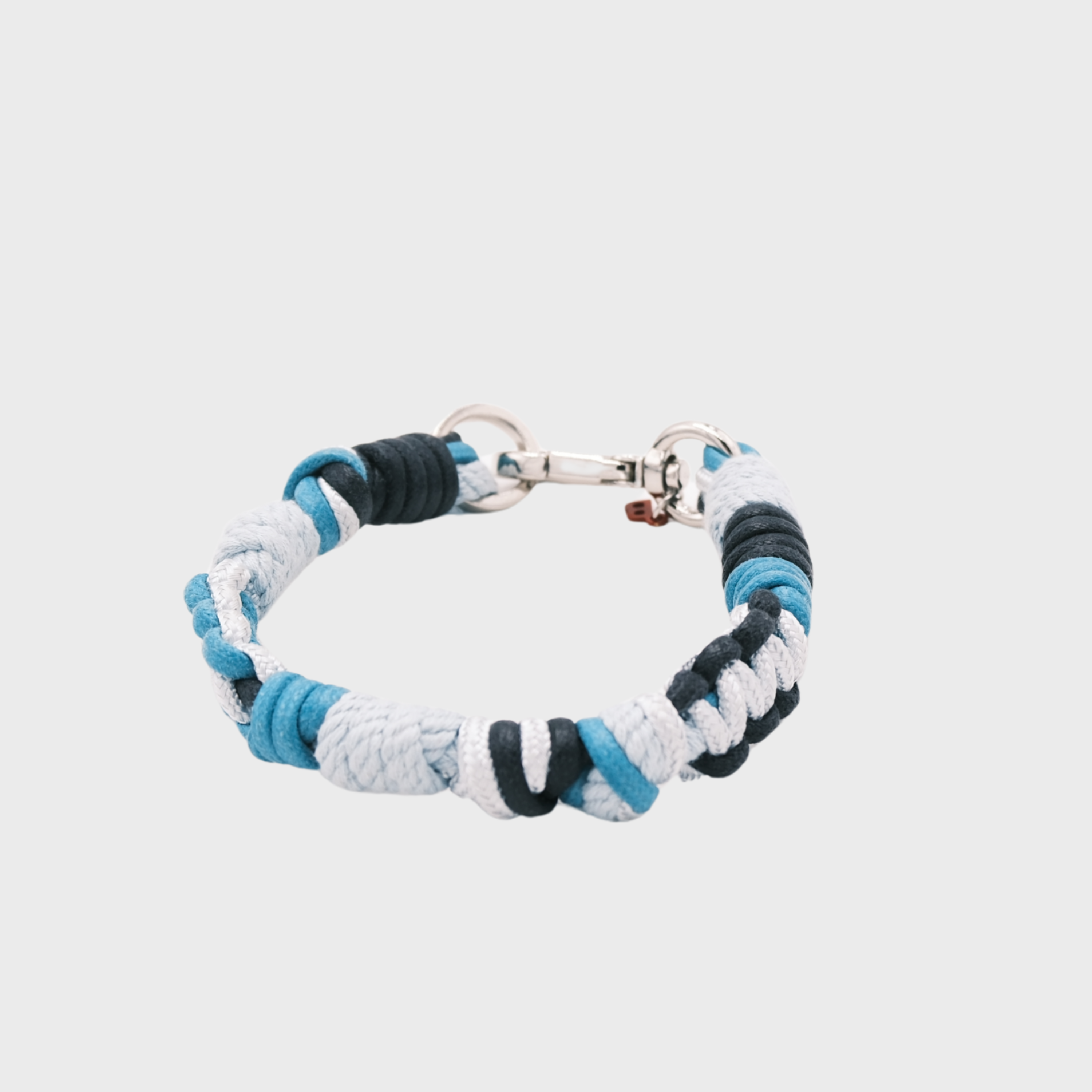 A braided macramé cord collar in shades of blue, dark blue and white with a silver clasp, centered on a light gray background.