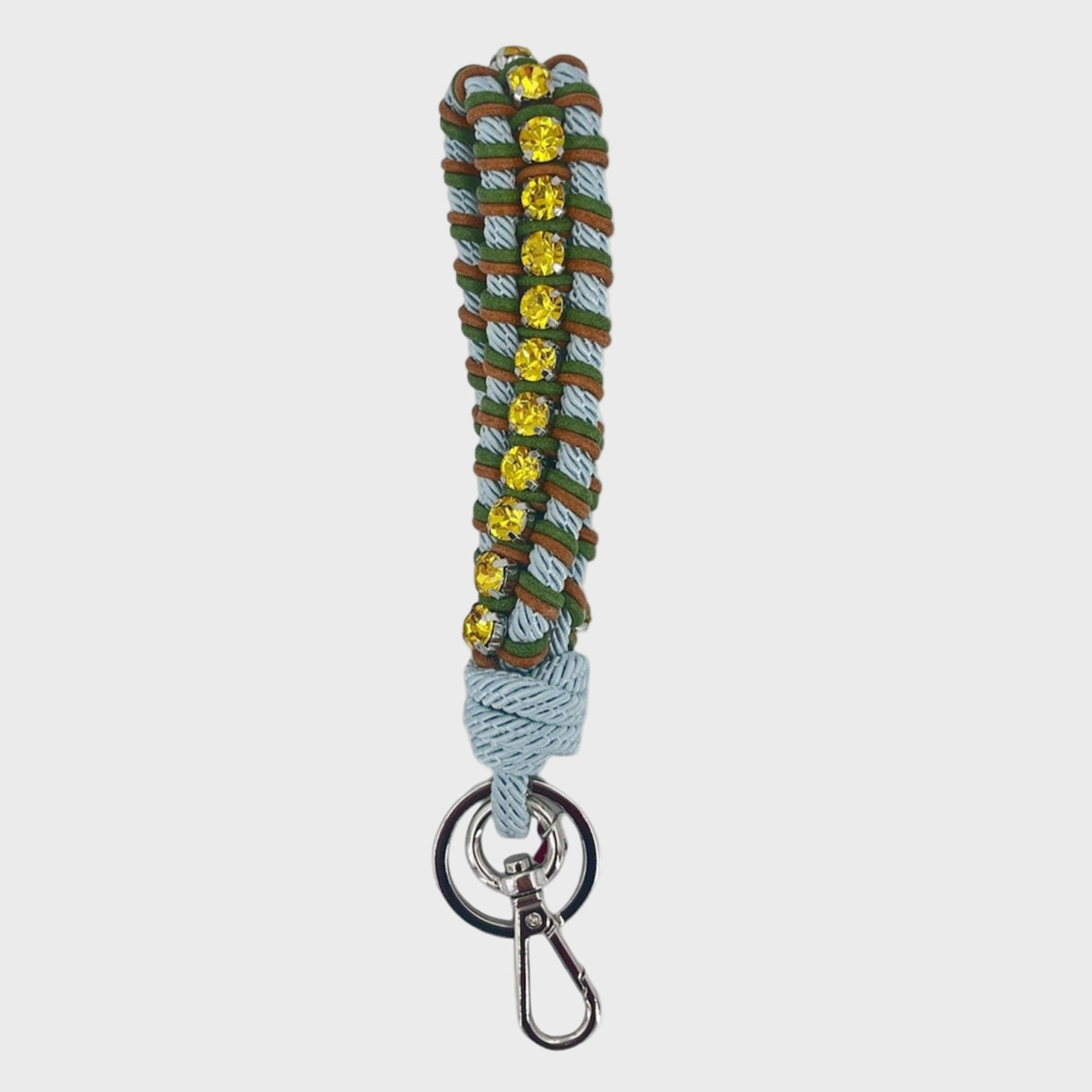 A macramé braided keychain strap featuring a blue, brown and dark green pattern, accented with a vertical row of yellow rhinestones, and finished with a silver metal lobster clasp on a light gray background.