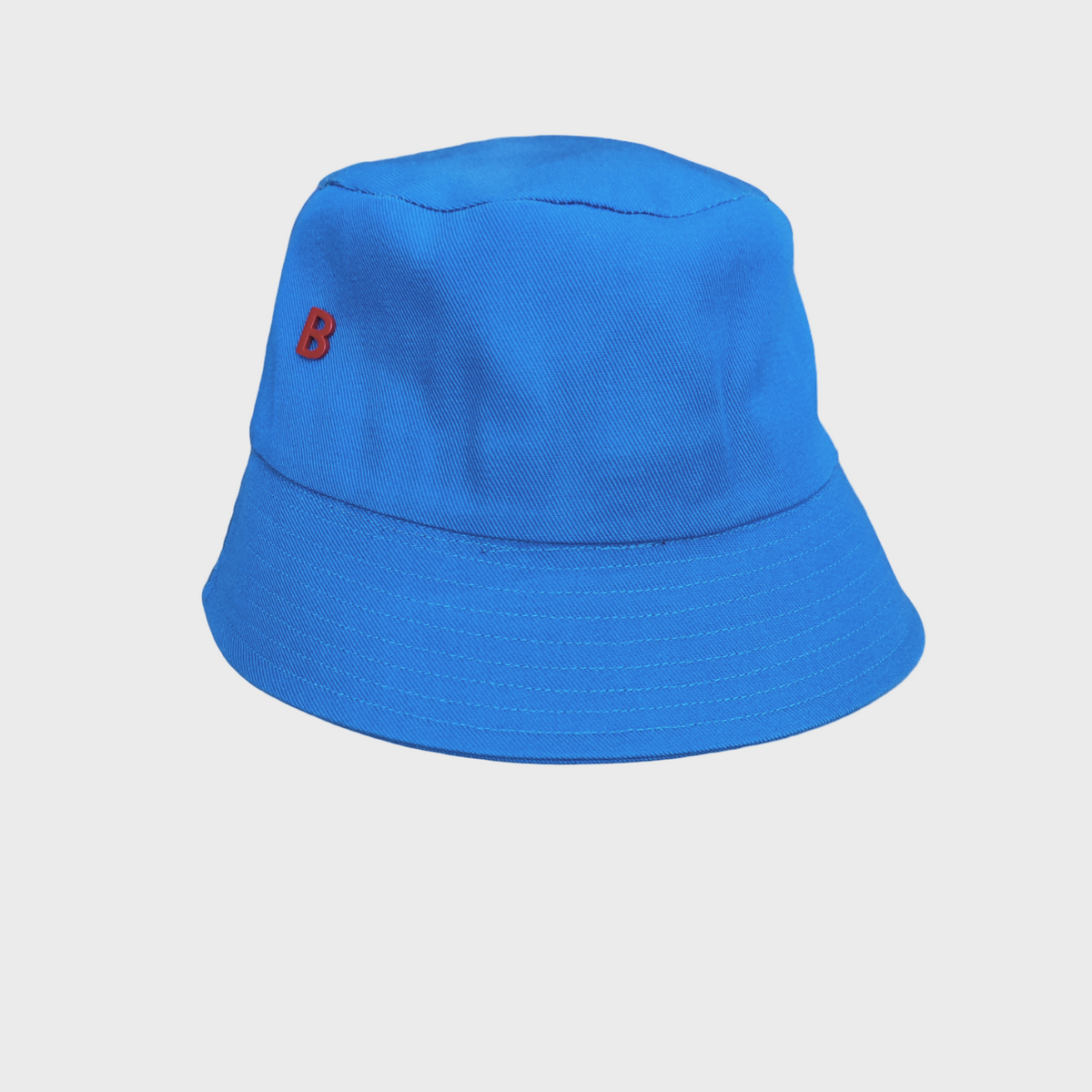 Blue bucket hat with a red B logo pinned on it on a light gray background