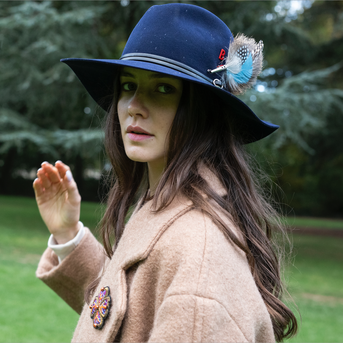 A woman wearing a blue hat accessorized with a blue feather brooch. 