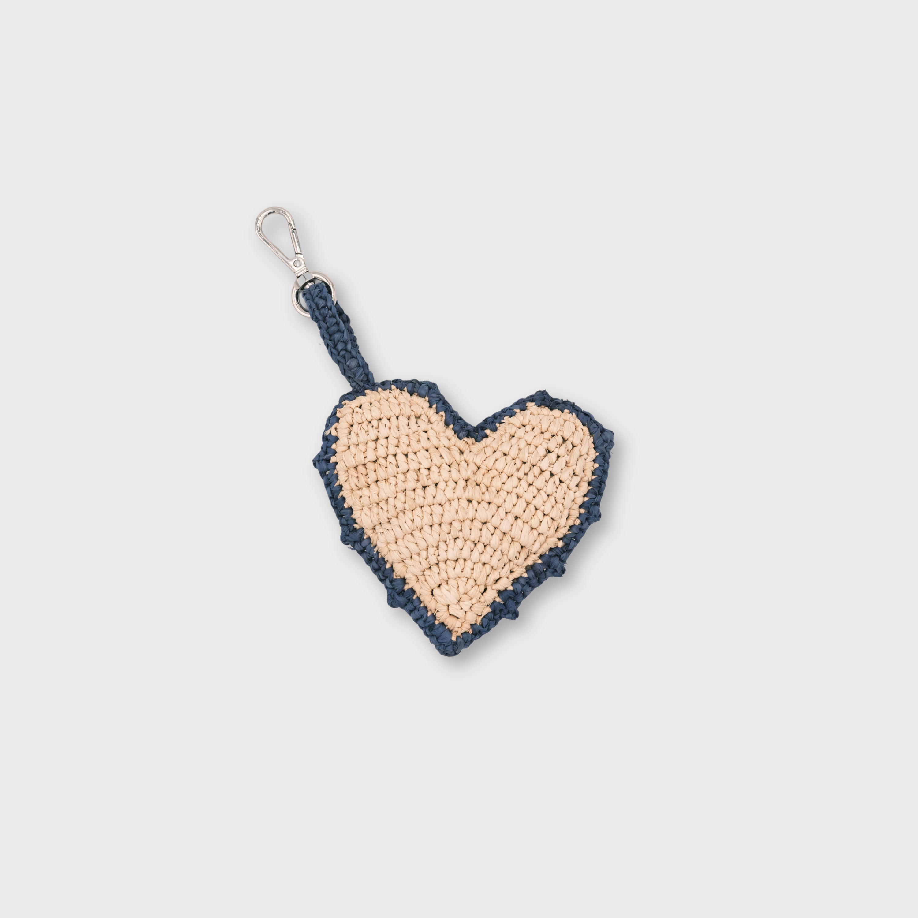 A heart-shaped raffia keychain in beige and navy blue rim, featuring a silver metal clasp.
