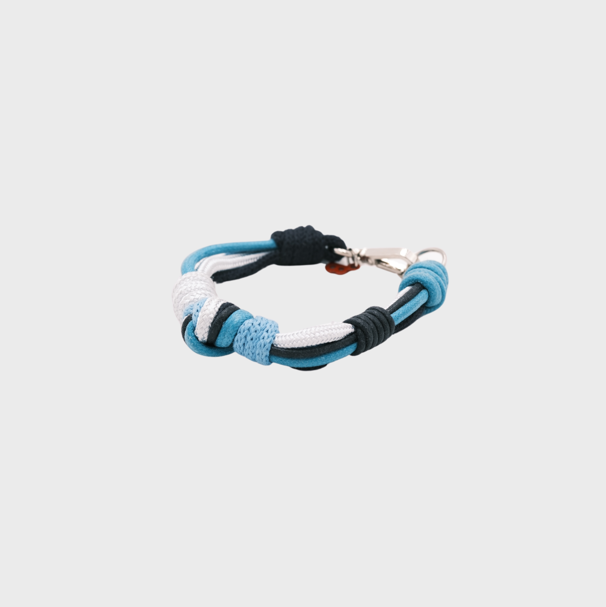 A macramé bracelet with knotted details, featuring shades of blue and white, finished with a silver-tone metal clasp, set on a light gray background.