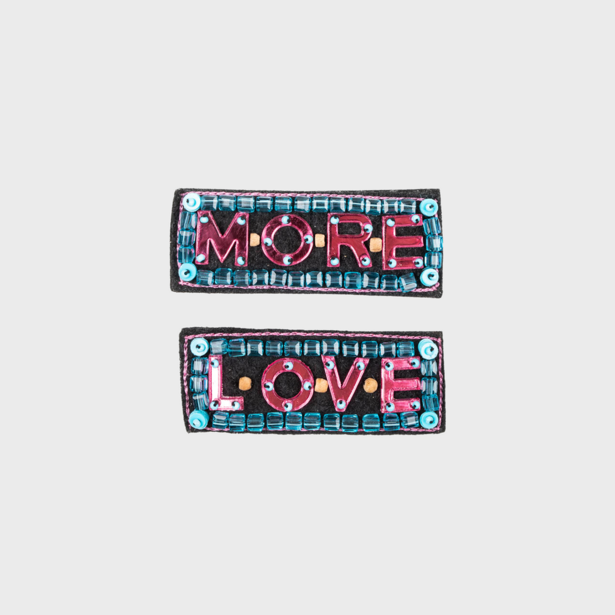 Two colorful embroidered brooches with 'MORE LOVE' text on a light gray background