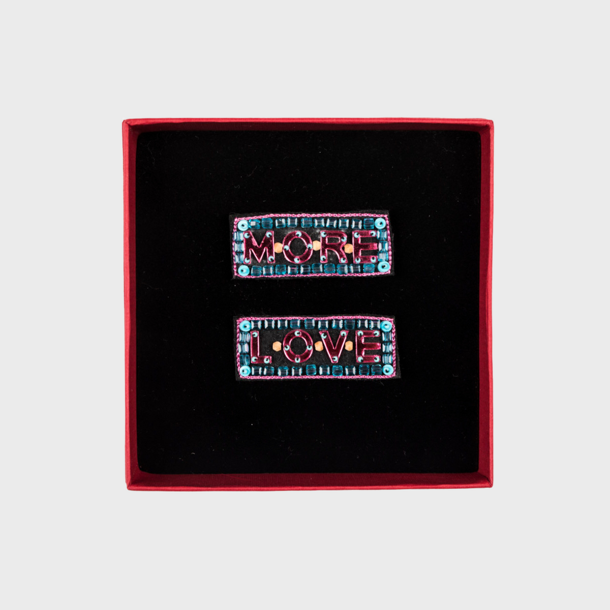 Two decorative brooches with 'MORE LOVE' text in a red box on a light gray background