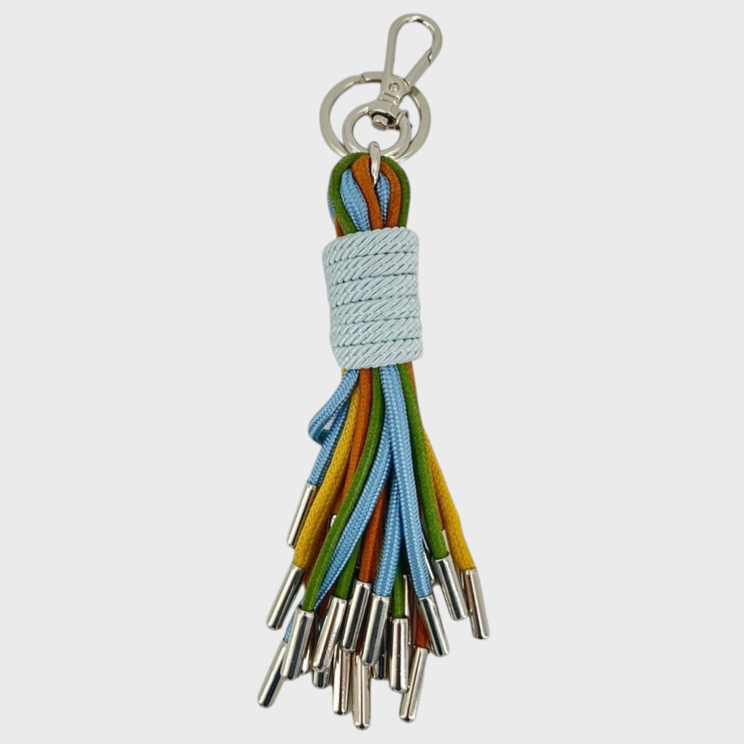 A keychain tassel with a silver metal clasp and ring, featuring a light blue woven wrap and multiple hanging cords in ocean blue, brown, mustard yellow and green. 