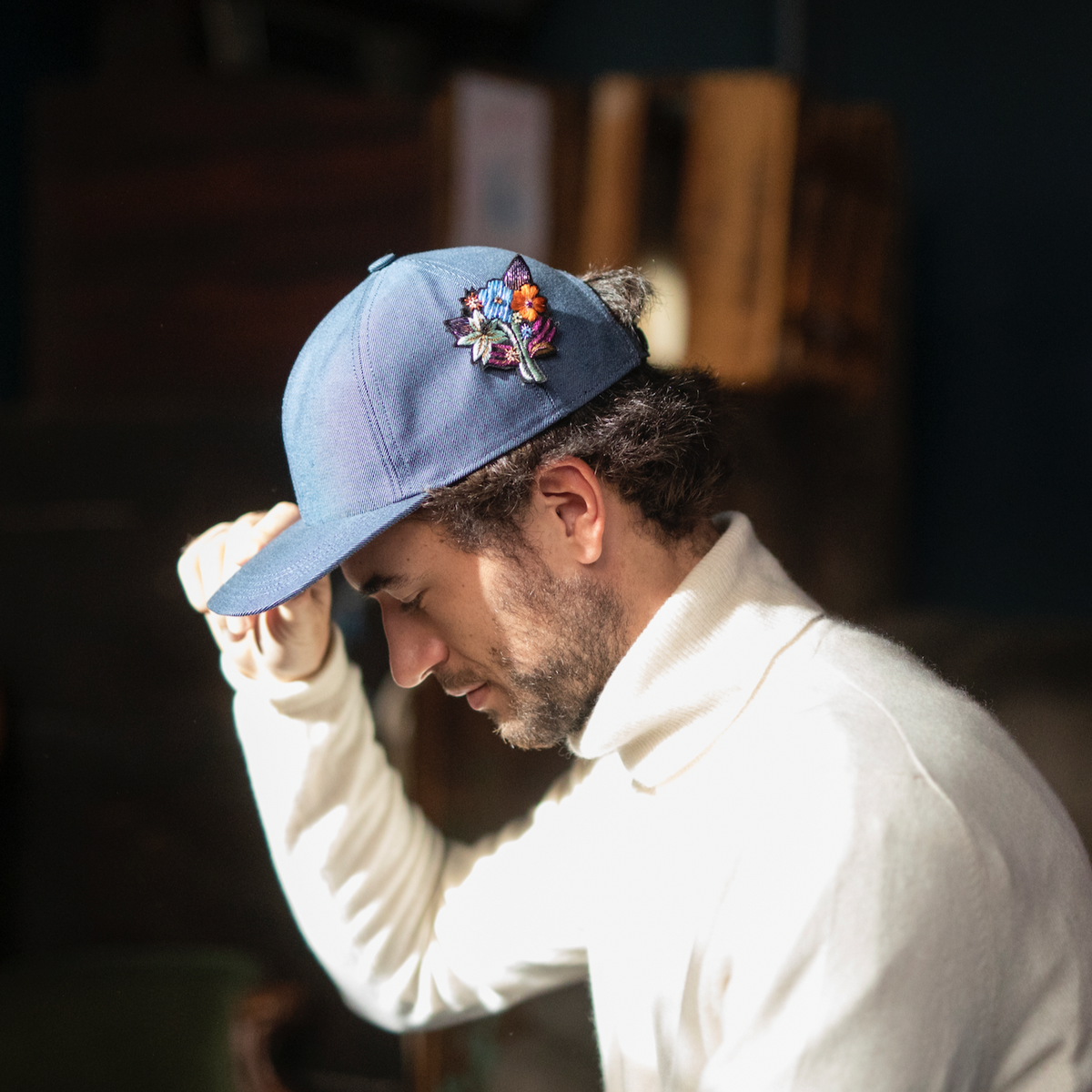 A person wearing a blue cap with a floral embroidered brooch on the front. 