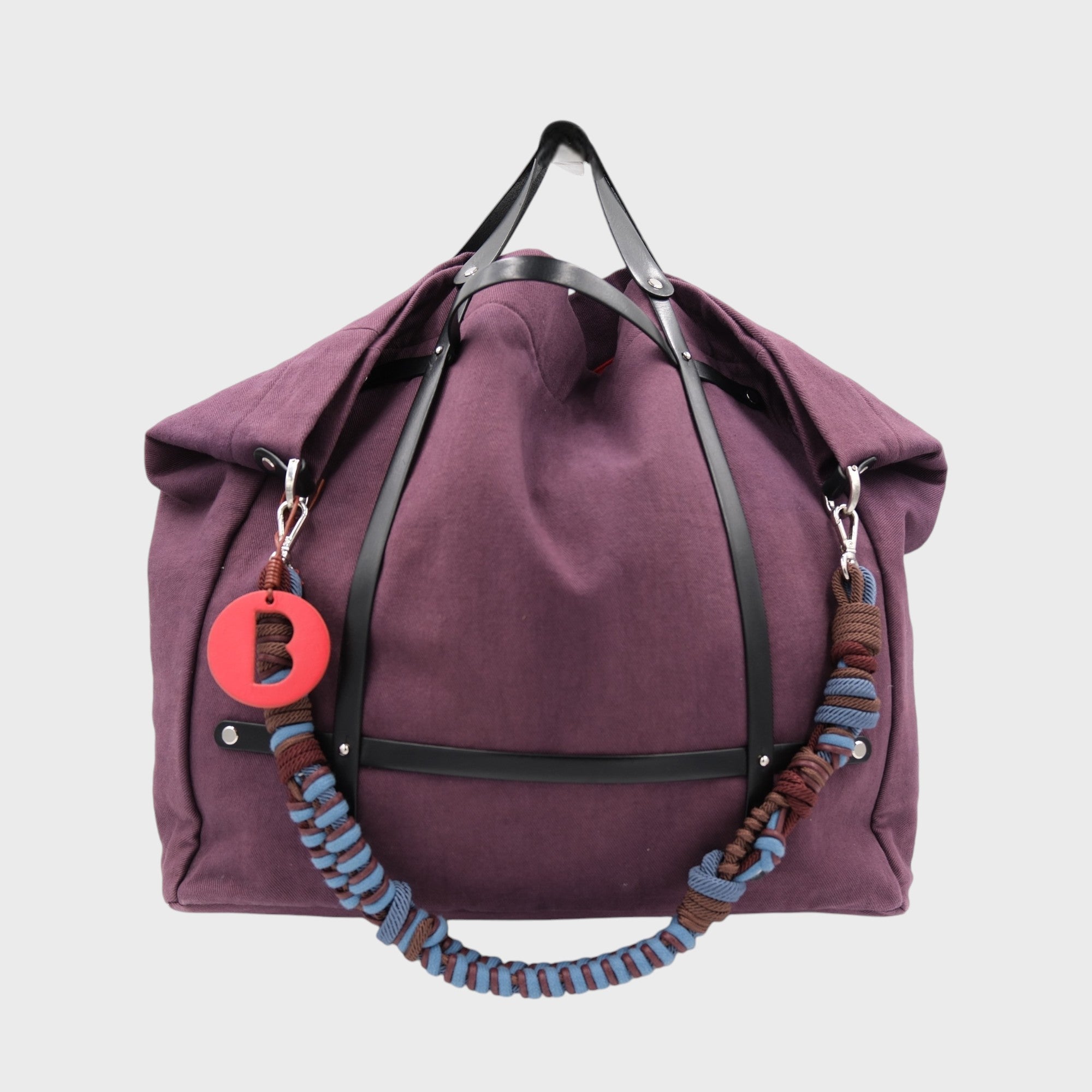 Purple aubergine weekend or duffle bag in canvas with black leather harness, paired with a colourful shoulder strap in blue and brown.