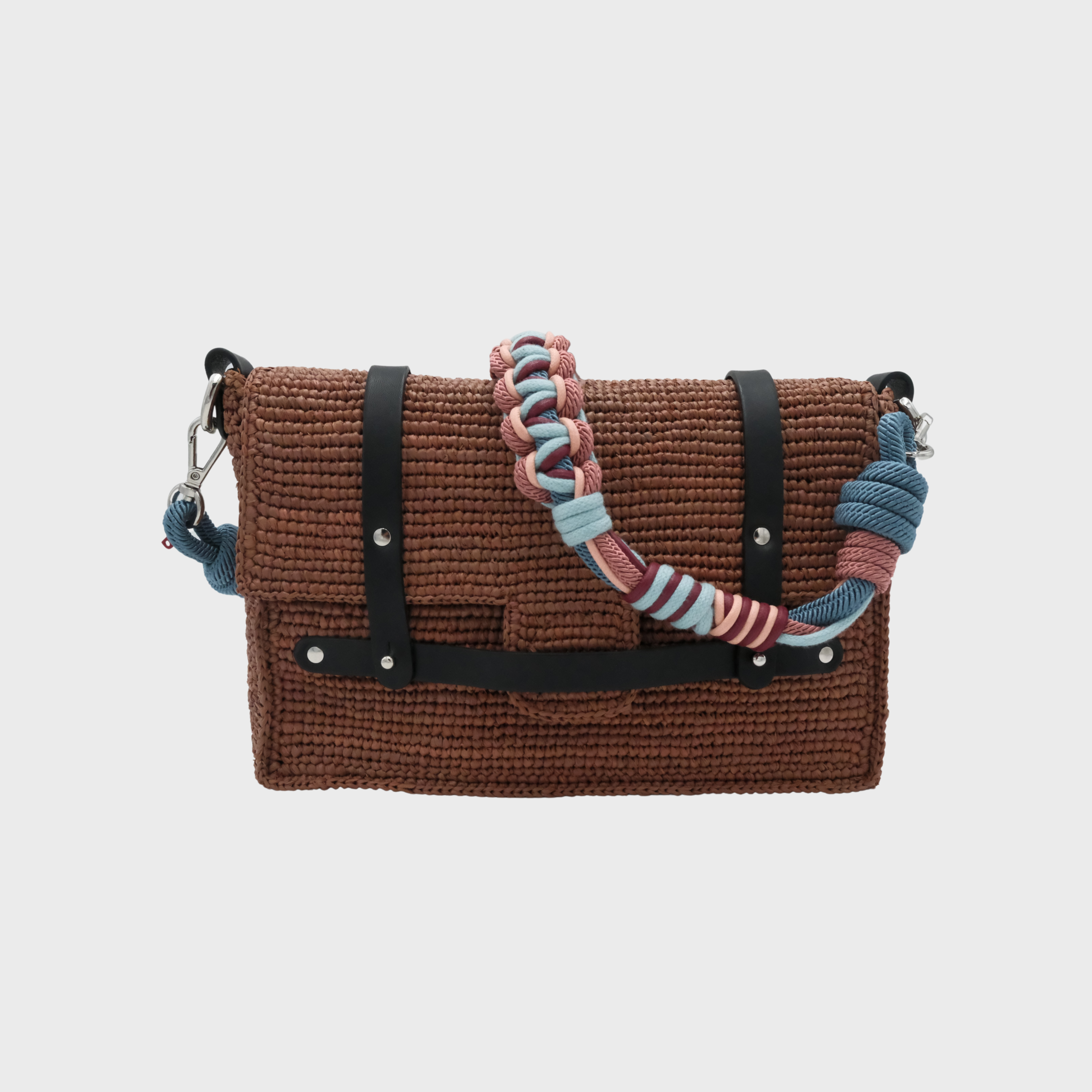A brown raffia shoulder bag with black leather straps and a colorful macramé braided strap featuring blue, pink, and white. 