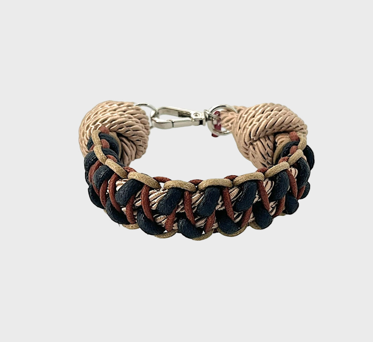 A braided macramé bracelet with shades of beige, black and brown. It ends and a silver clasp, shown on a light gray background.