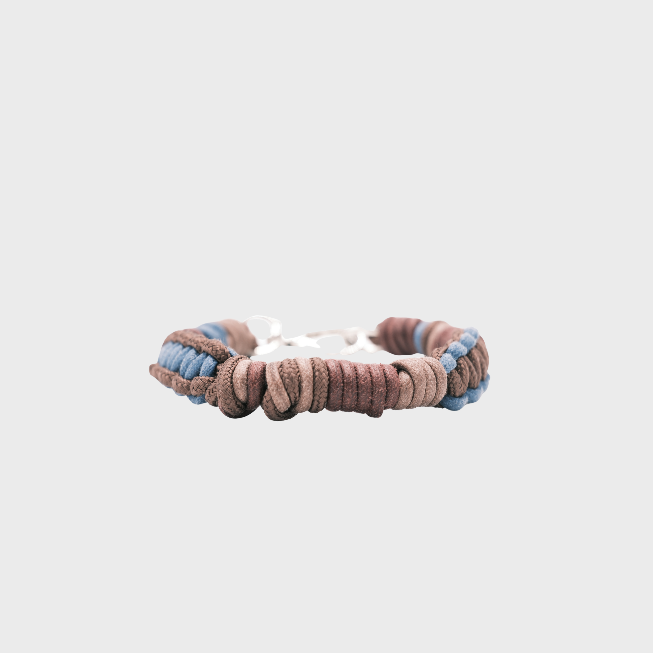 A handmade braided macramé collar in shades of brown and blue with a silver clasp, centered on a light gray background.