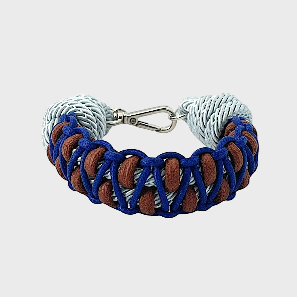 A braided macramé bracelet with shades of dark and light blue and brown. It ends and a silver clasp, shown on a light gray background.