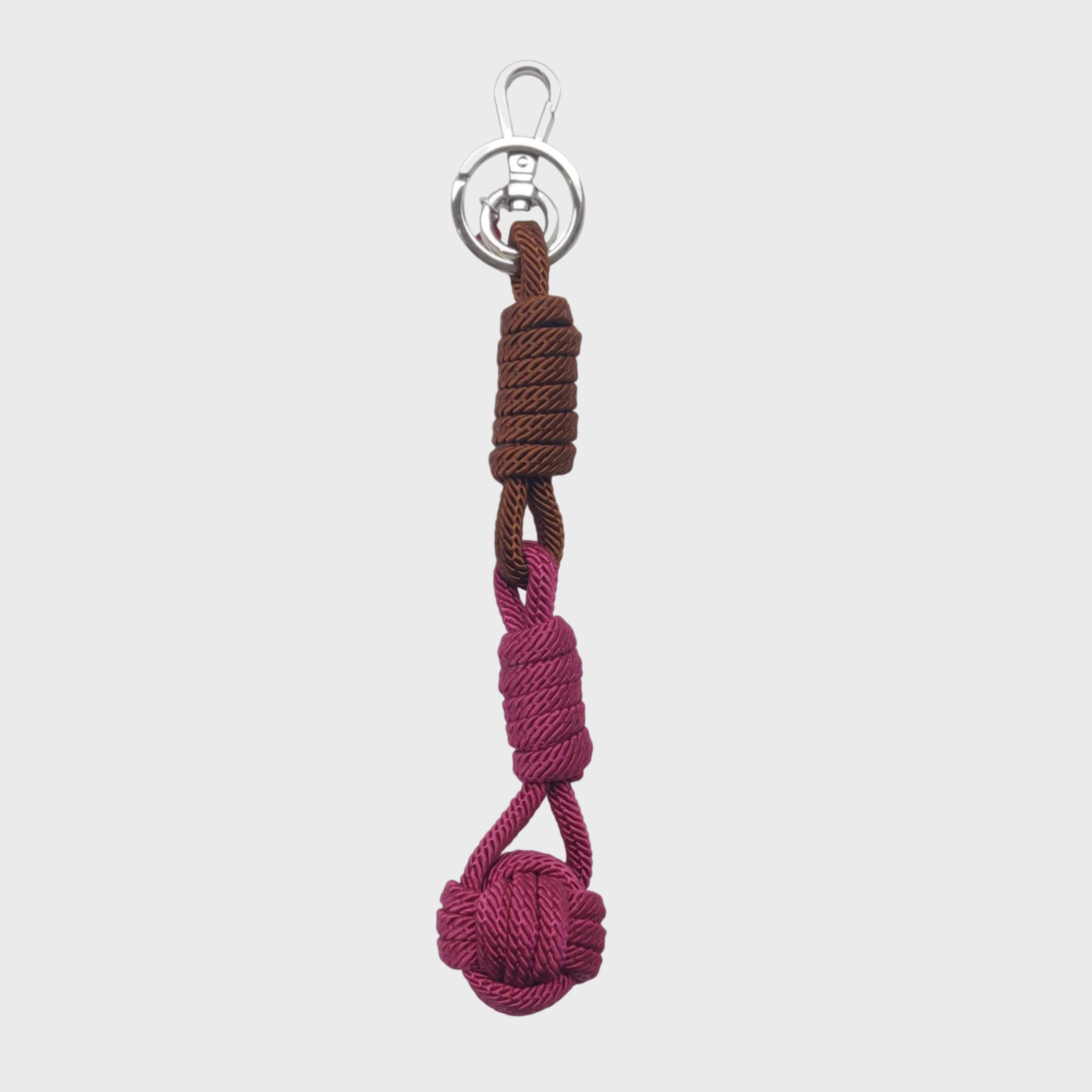 A macramé keychain representing a ball inspired by sailors knots. The straight upper part is brown and the ball part is fuschia. 