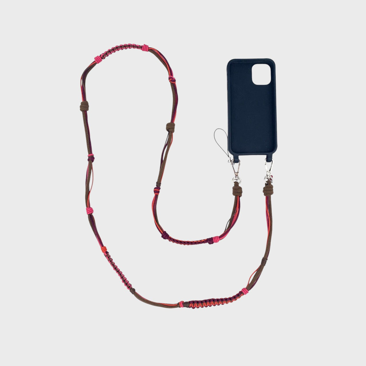Pink, red and brown macramé woven phone lanyard with a black phone case on a white background. 