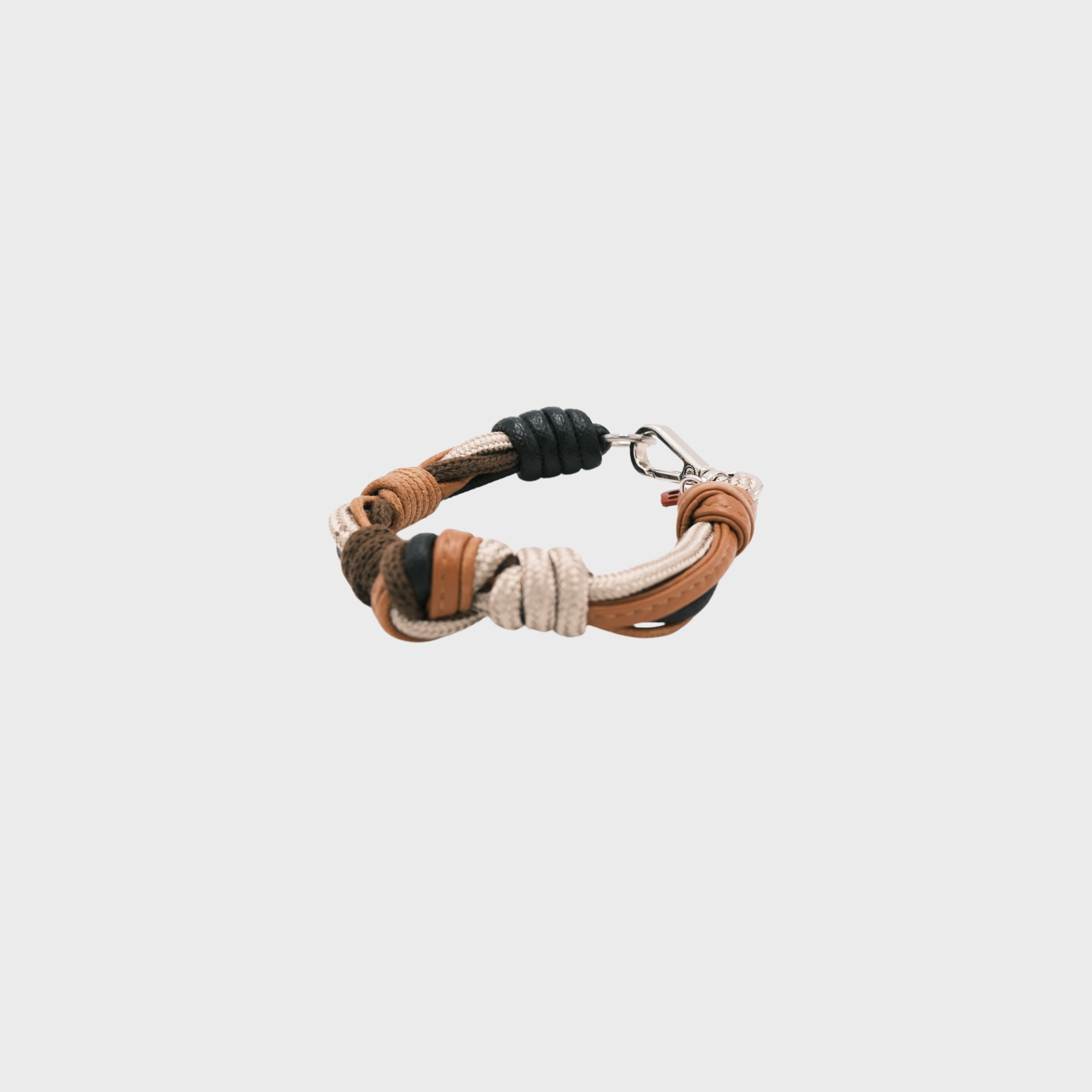 A leather and rope bracelet with knotted details, featuring shades of brown, beige, and black, finished with a silver-tone metal clasp, set on a light gray background.