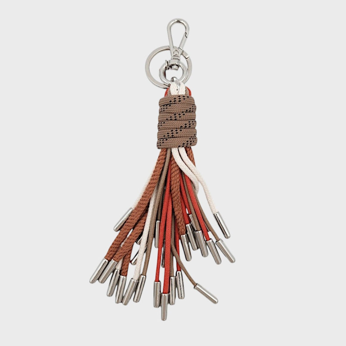 A keychain tassel with a silver metal clasp and ring, featuring a brown woven wrap and multiple hanging cords in brown, white, and orange.