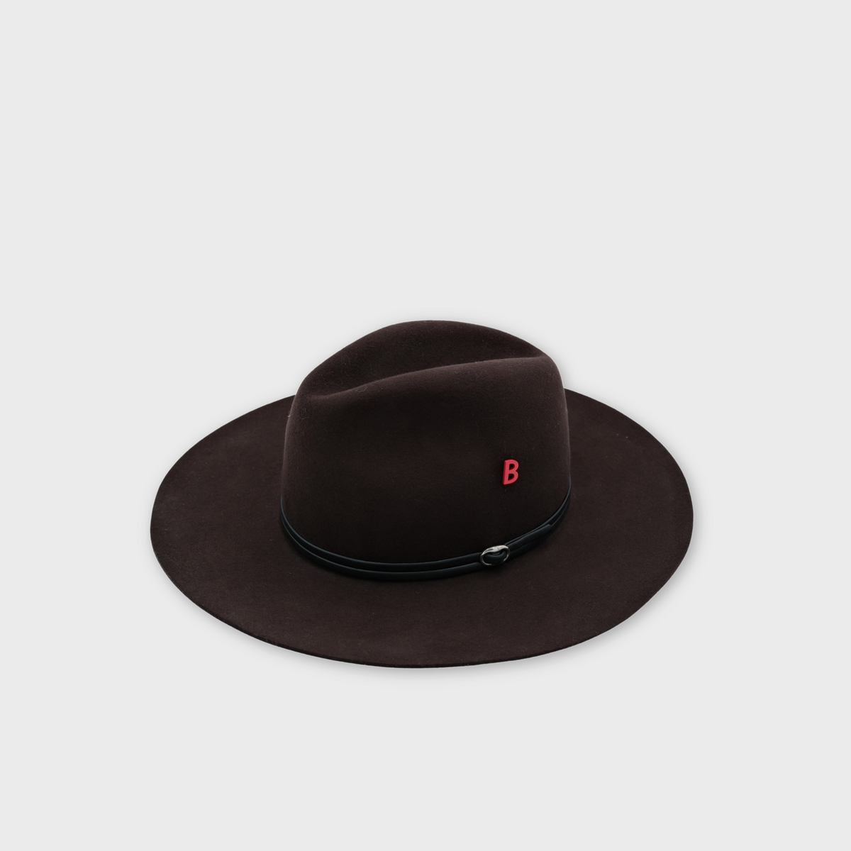 A dark brown felt fedora hat with a black band and a small red letter 'B' pin on the side, shown against a light gray background.