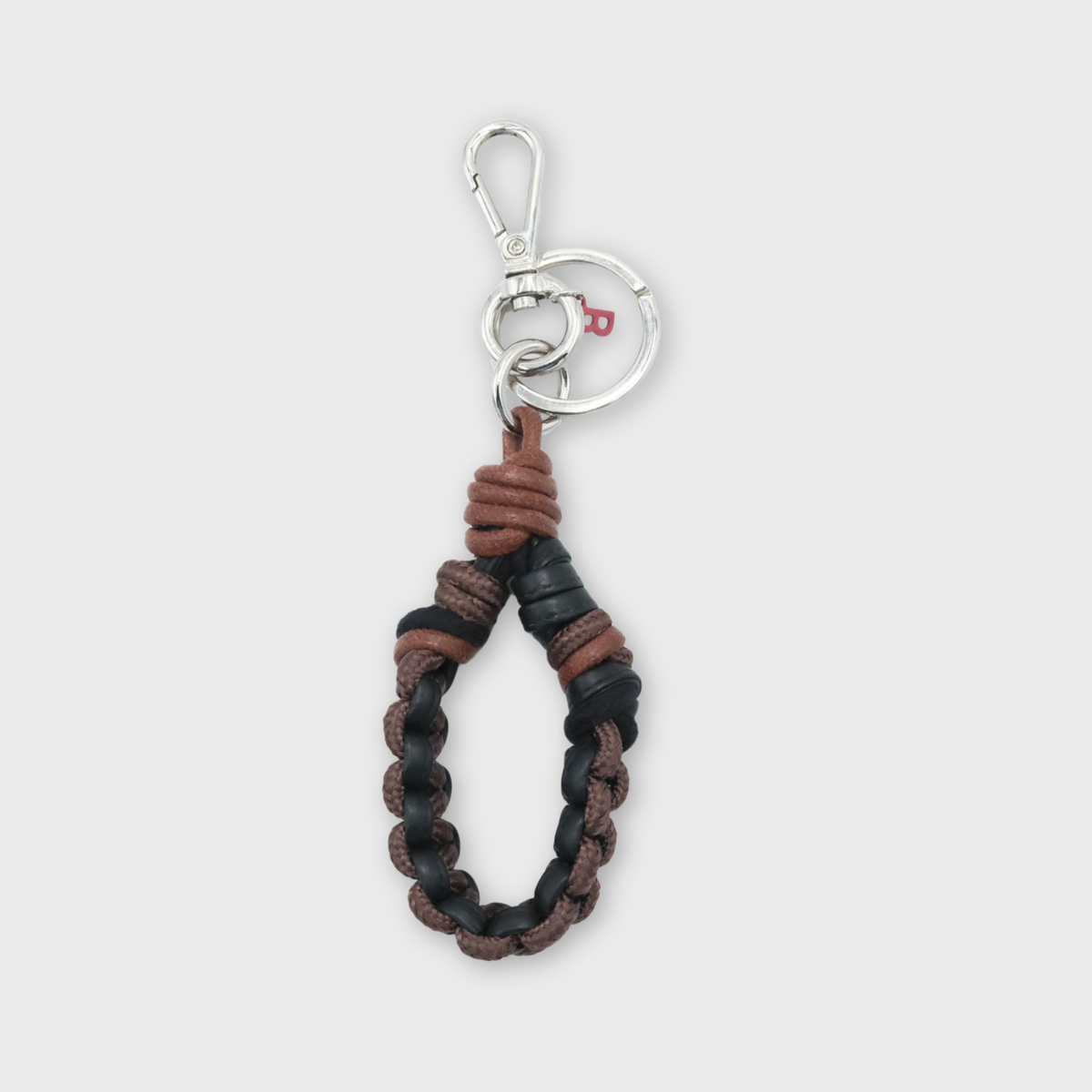 A knotted macrame keychain featuring a braided design in brown and black leather, finished with a silver metal clasp, set against a light gray background.