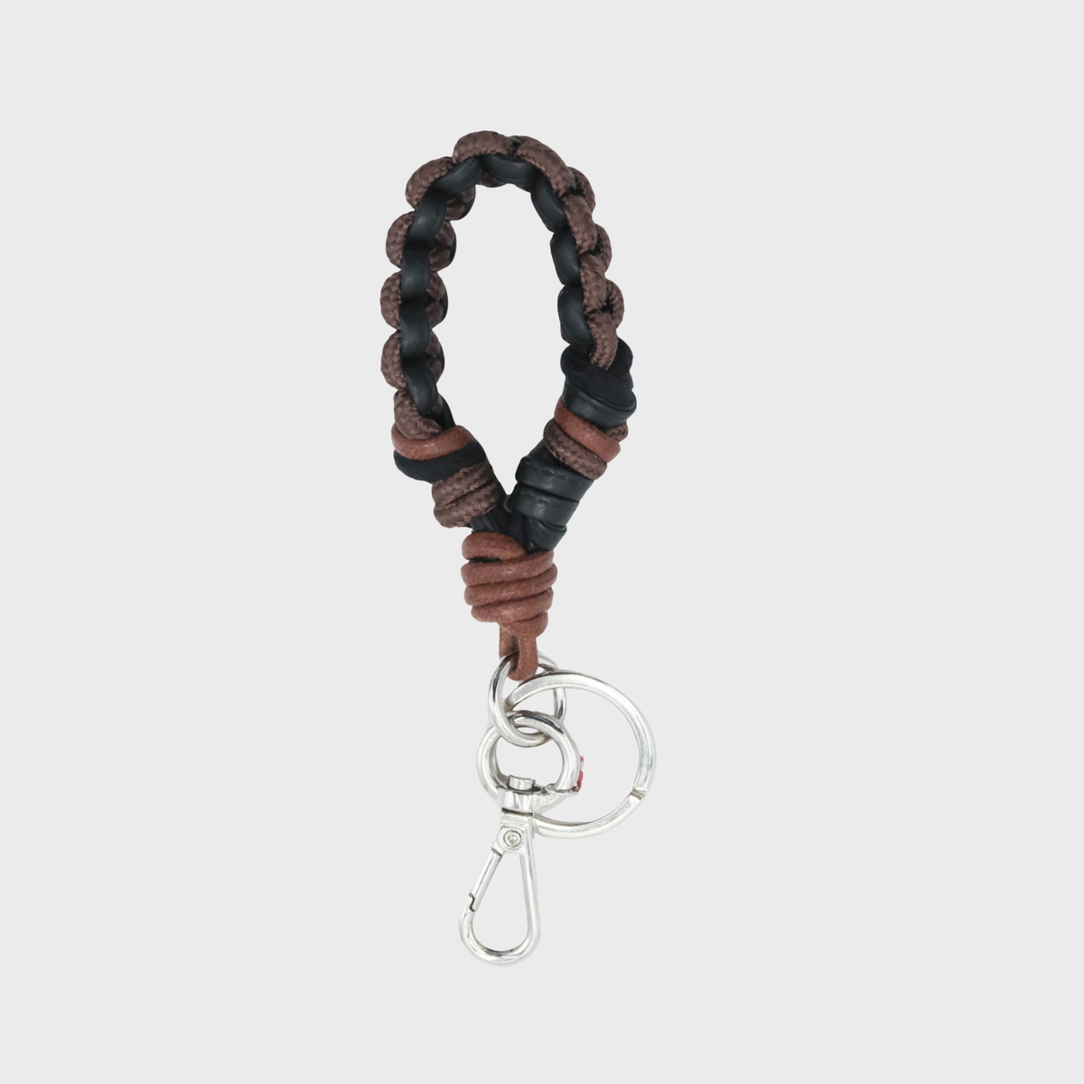 A knotted macrame keychain featuring a braided design in brown and black leather, finished with a silver metal clasp, set against a light gray background.