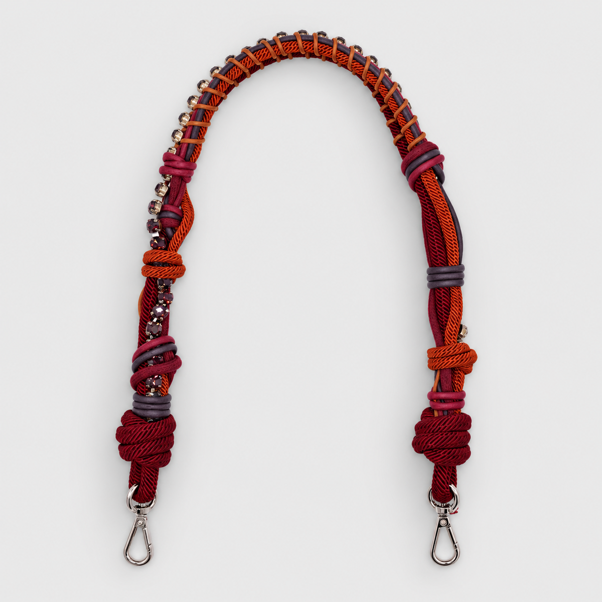 A burgundy macramé bag strap with purple rhinestones on a light grey background. 