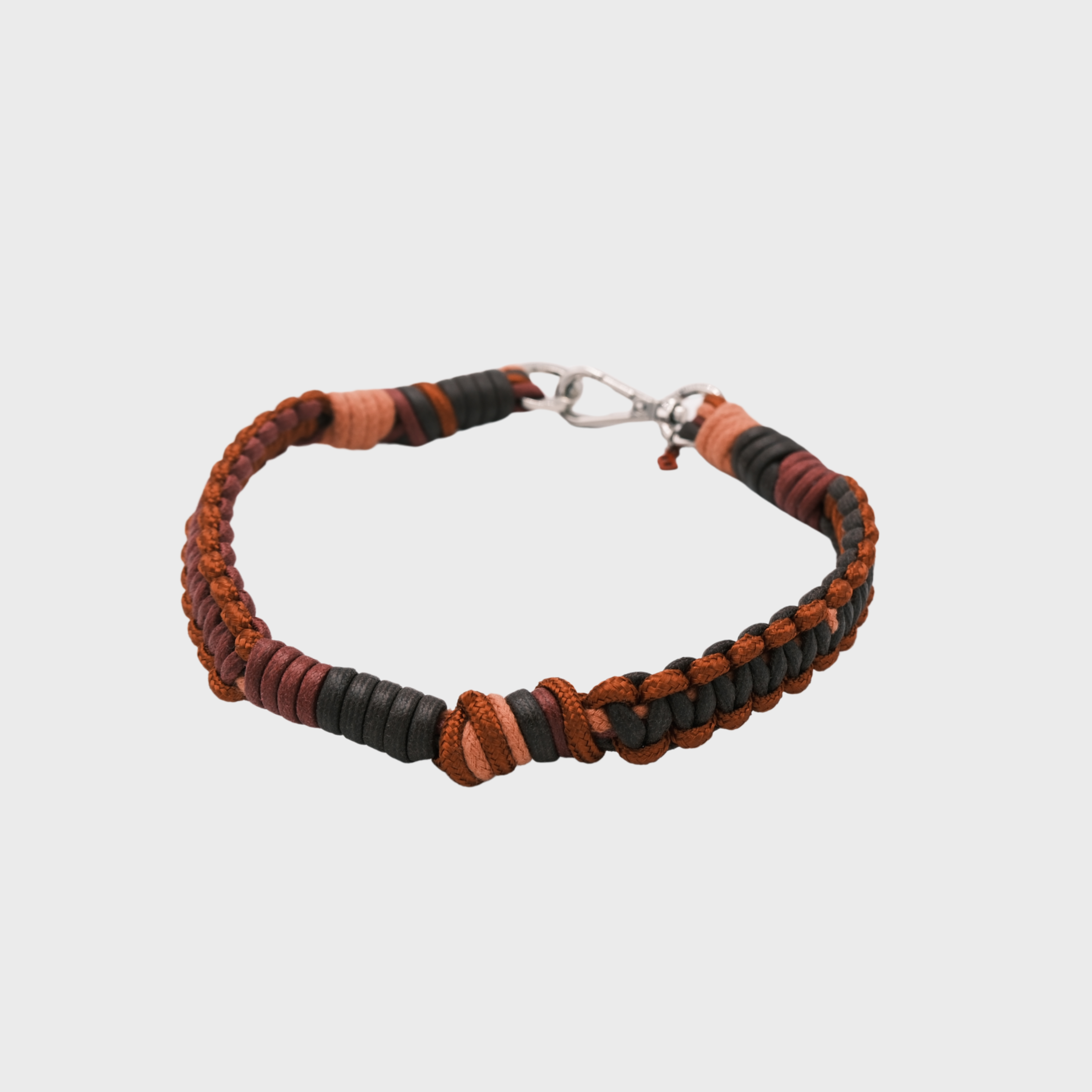 A braided macramé cord collar in shades of burgundy, black and light brown with a silver clasp, centered on a light gray background.