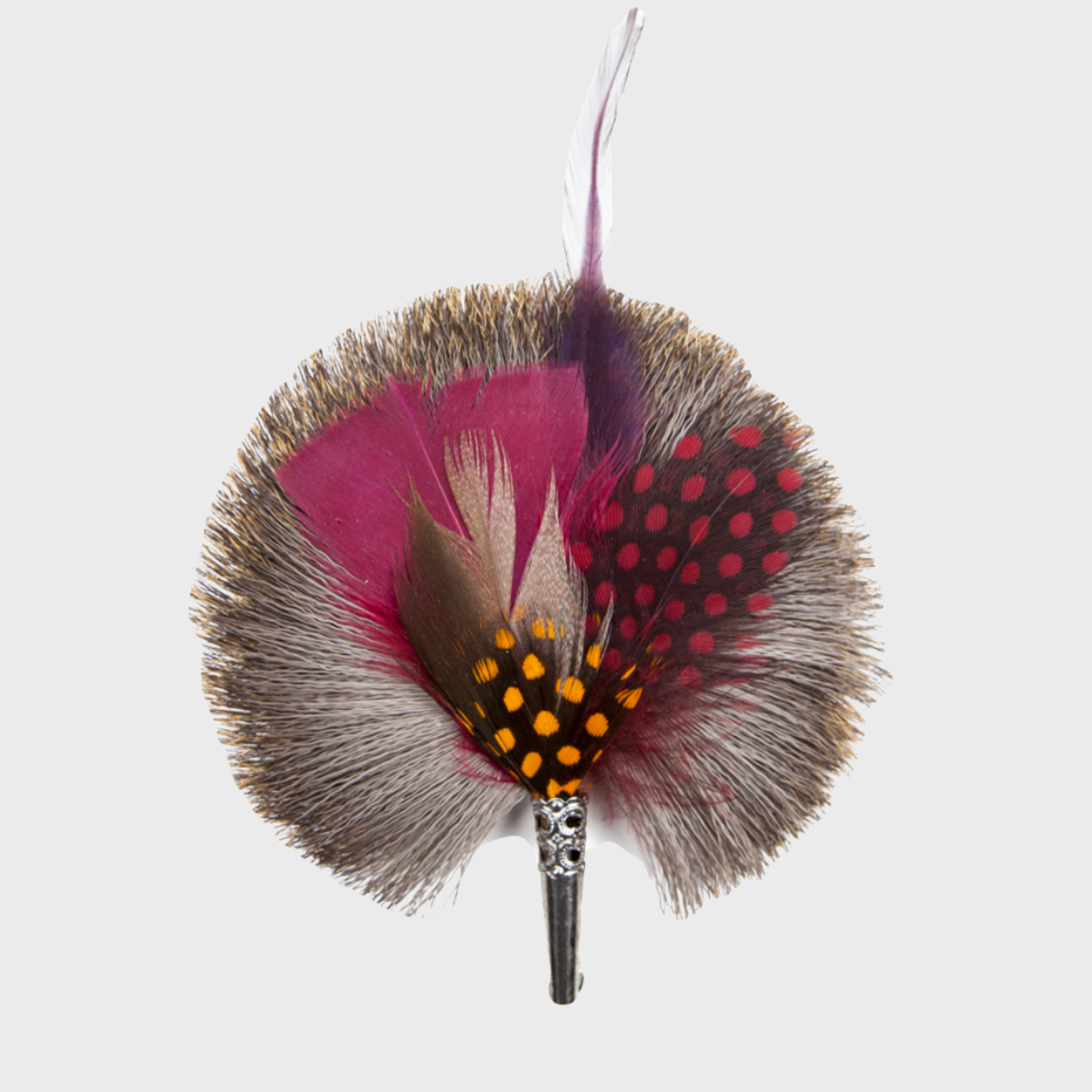 A round brooch featuring a central pin with attached feathers in various shades of pink, red, and gray, with decorative dots around the perimeter.