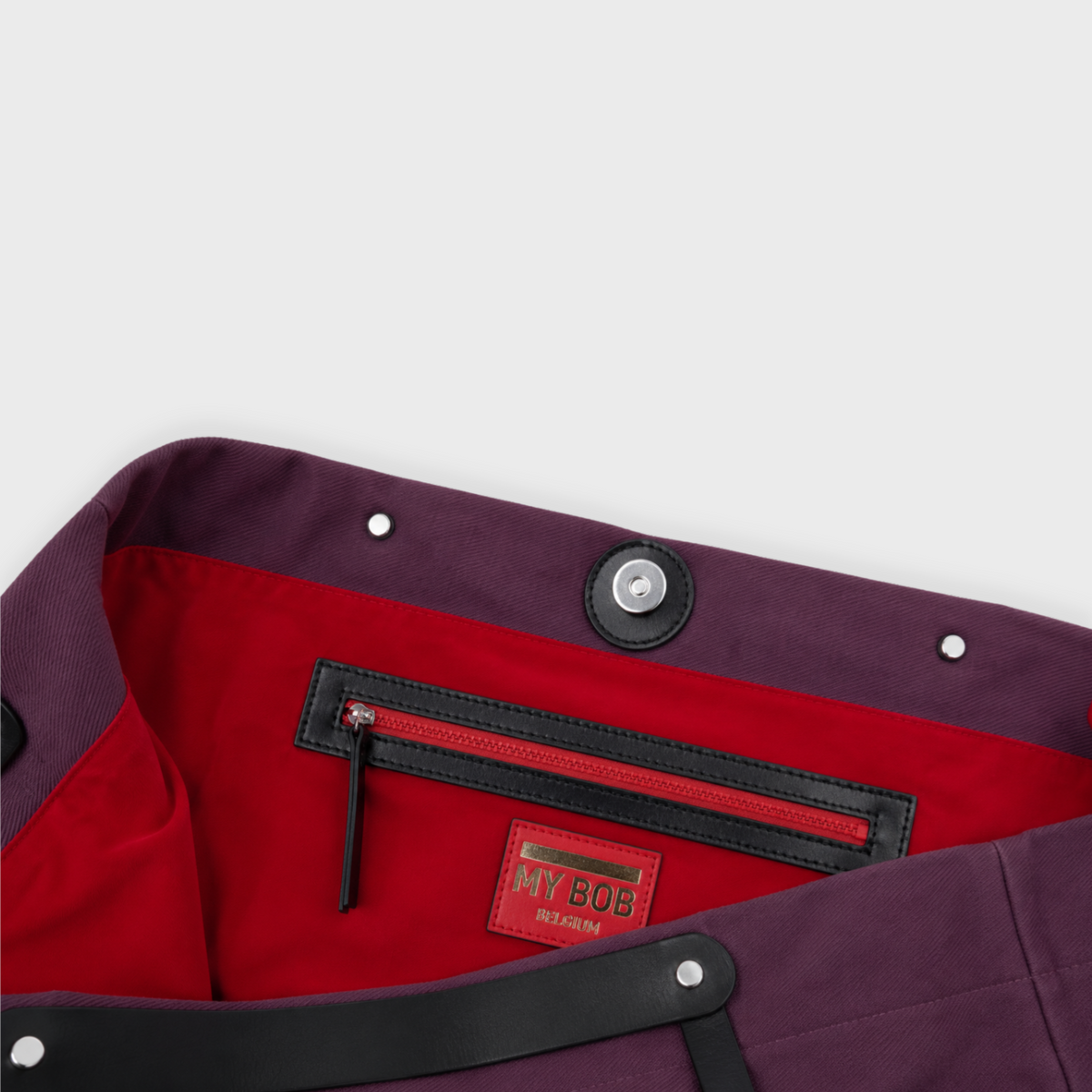 Close-up of a dark purple cotton bag with a bright red interior lining, featuring a black zippered pocket and a red 'MY BOY BELGIUM' brand patch.