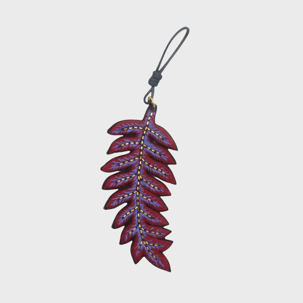 An embroidered Purple leaf-shaped keychain with a grey cord on a light gray background