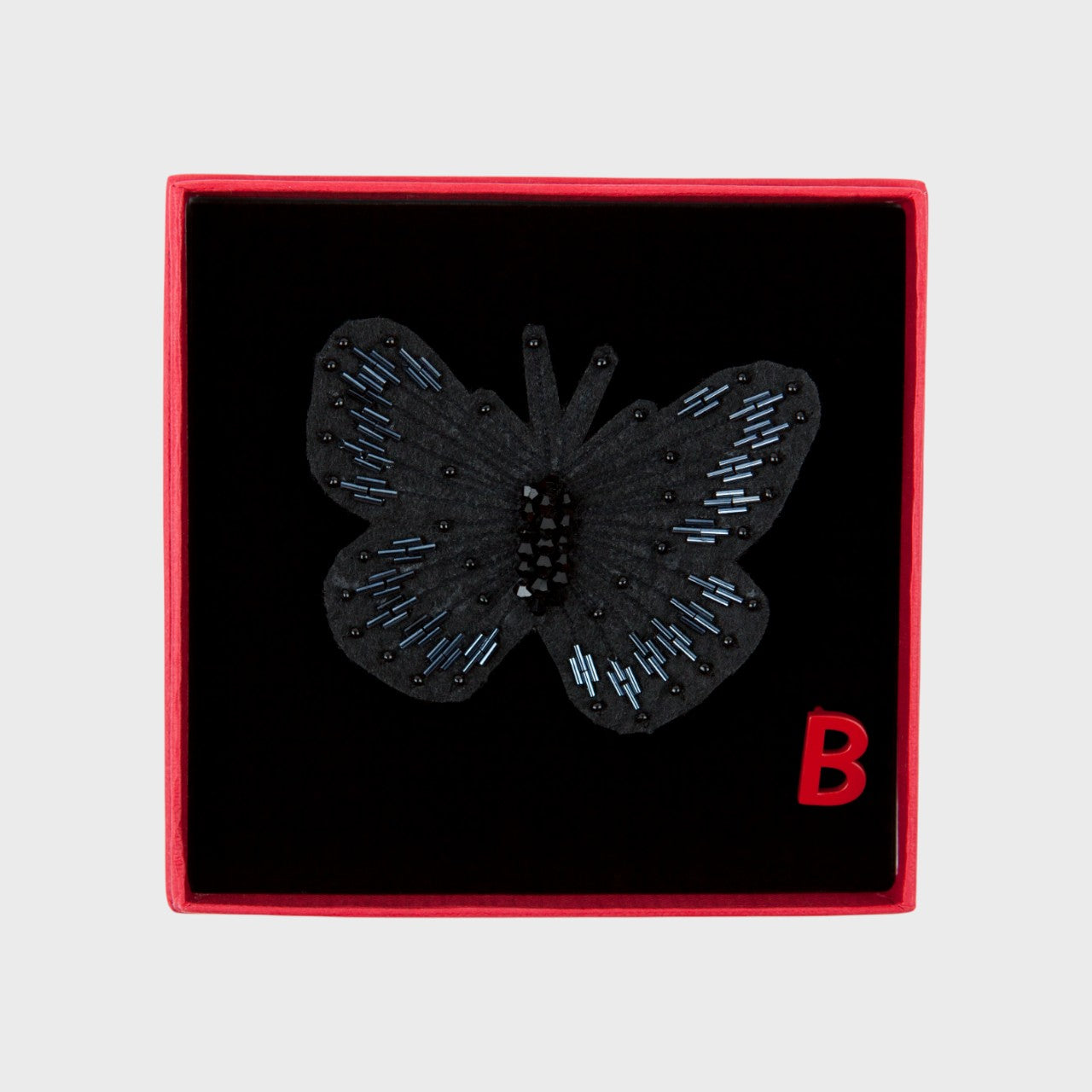 An embroidered brooch representing a black butterfly in a box. 