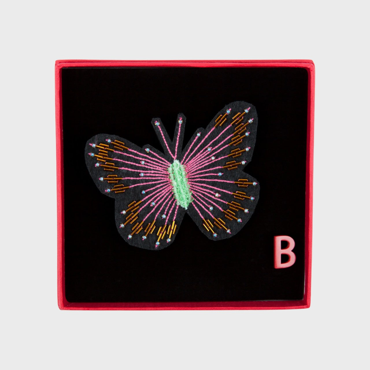 An embroidered brooch representing a pink butterfly in a box. 