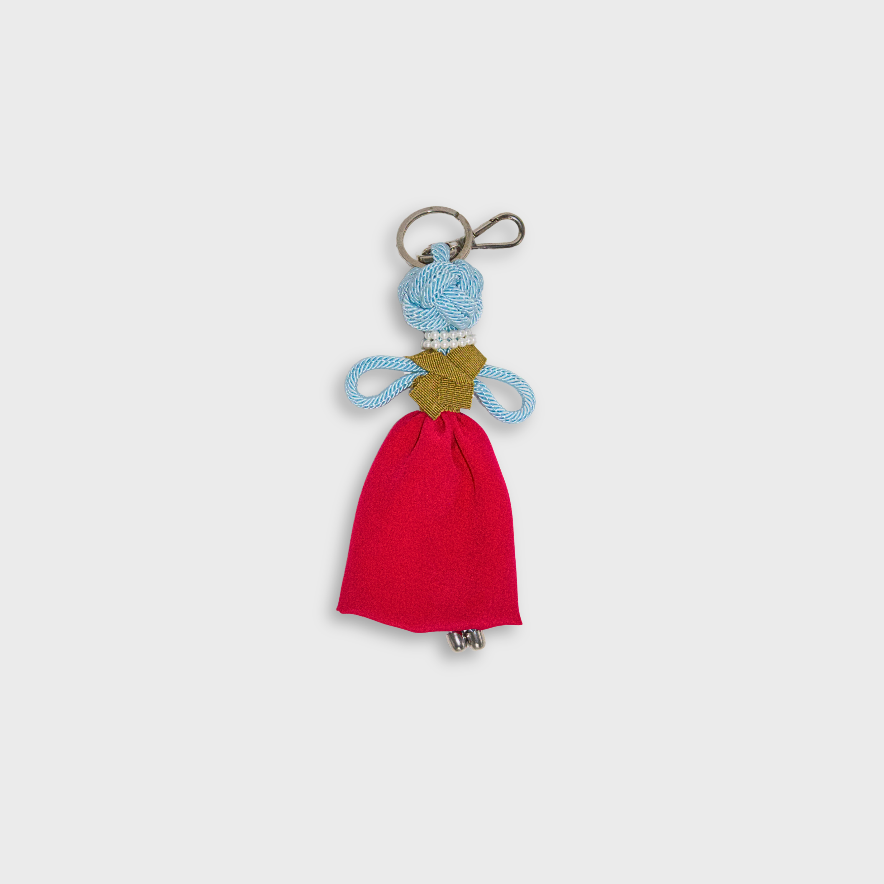 A handmade blue macramé doll keychain featuring a bright pink maxi skirt, a mustard yellow top, a doubled pearl necklace, and a silver metal keyring.