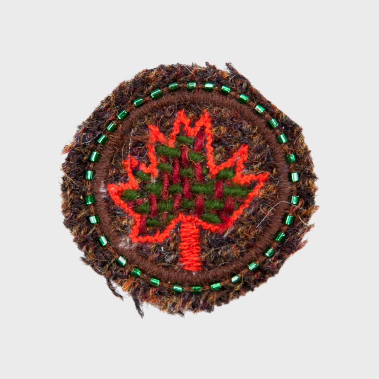 An embroidered brooch representing the Canada leaf in red, in the middle of a circle. 