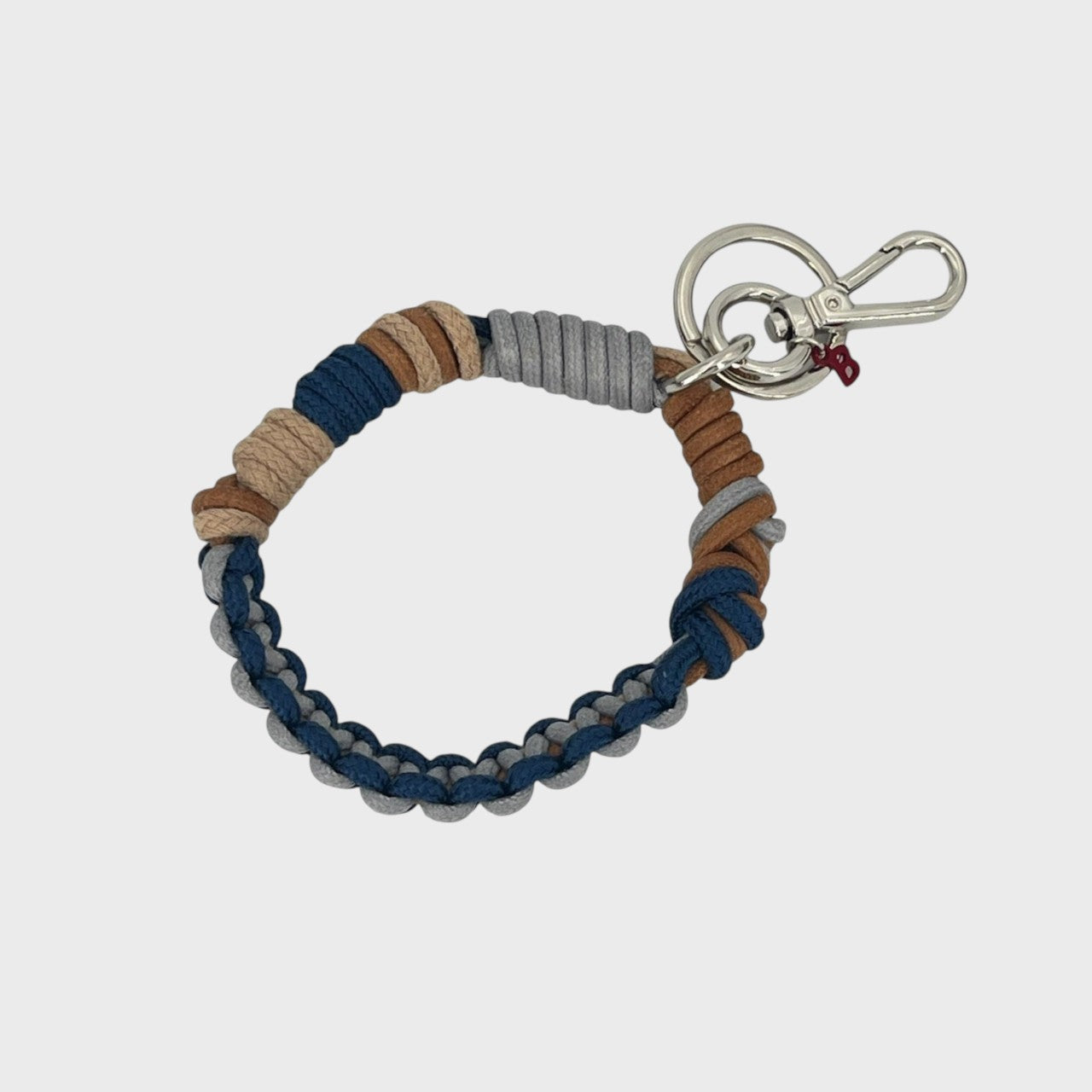 A woven macramé key chain with grey, beige, brown and ark blue patterns, inspired by celtic knots, finished with silver-tone metal hardware.